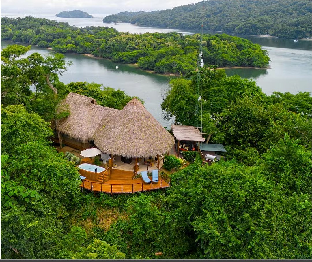Aerial view of a thatched-roof eco-lodge nestled in tropical rainforest above a river bay in Central America