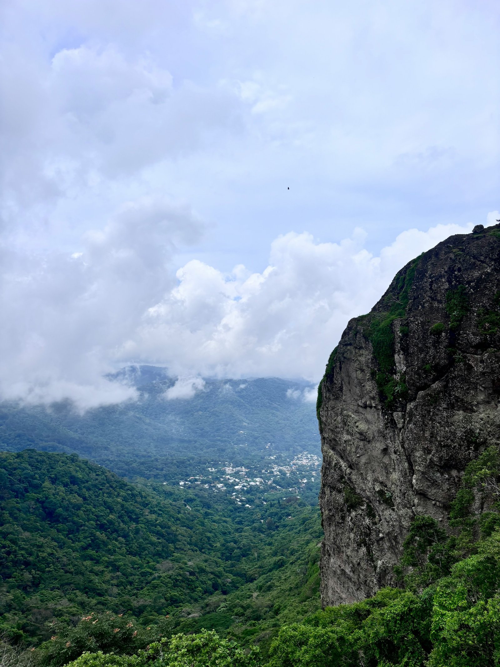 Dramatic cliff face above lush green valleys and a small town in the clouds, El Salvador