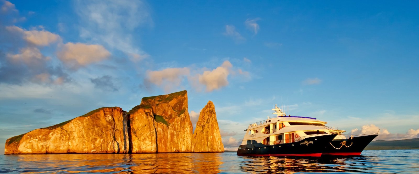 Private expedition yacht anchored off a remote Galápagos island with sea lions on volcanic rock in the foreground