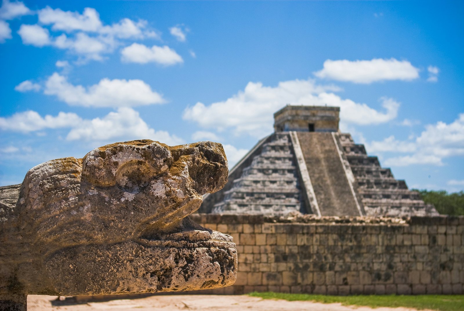 Stone serpent head at Chichén Itzá with El Castillo pyramid in the background