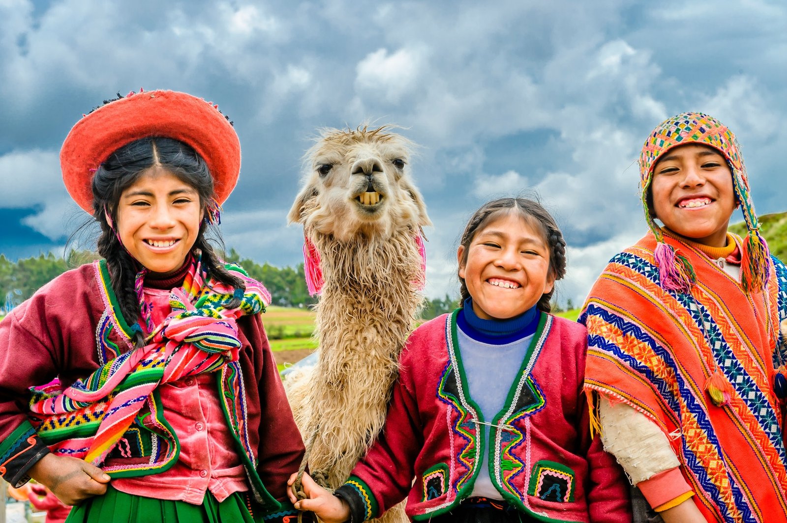 Children in traditional Andean dress smiling with a llama near Cusco, Peru
