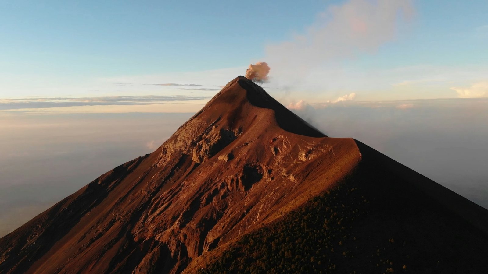 Volcán de Fuego erupts with a plume of ash and smoke at sunrise, viewed from the summit of Acatenango